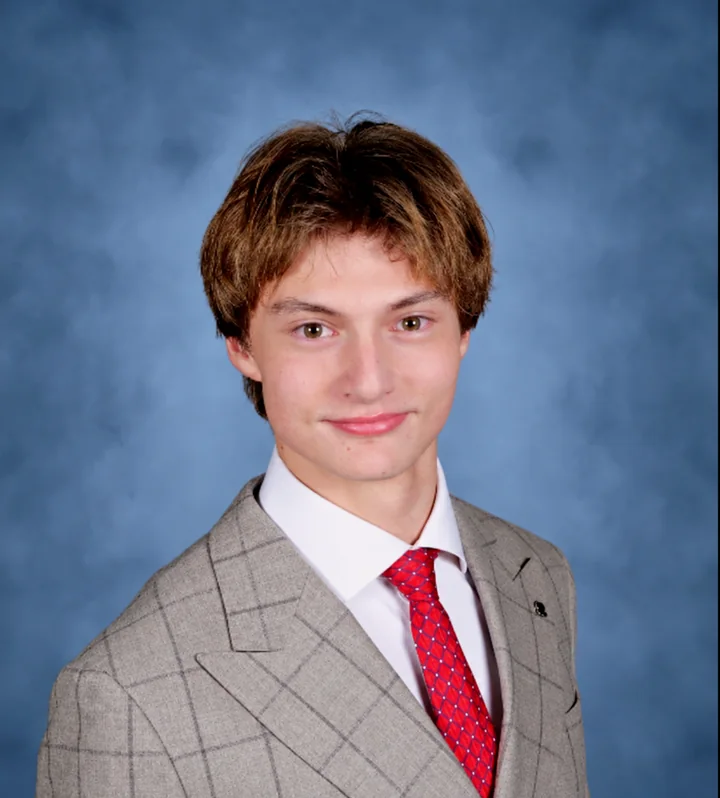 Georgii Demkin in a gray suit and red tie against a blue background